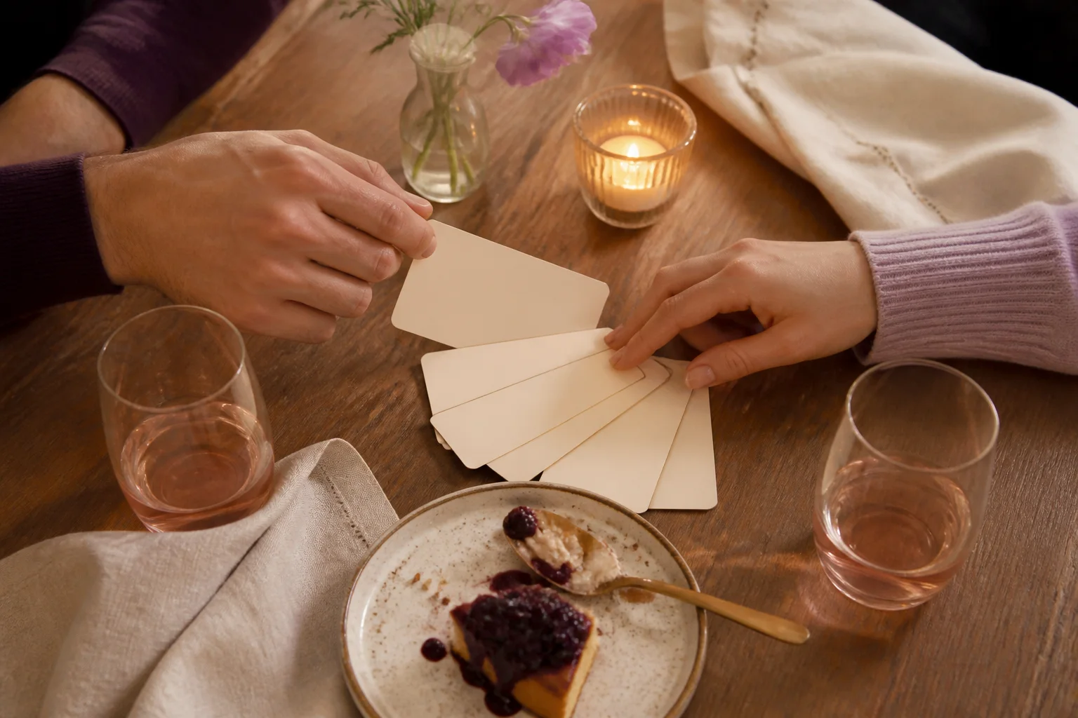 Two people choosing blank question cards across a candlelit table